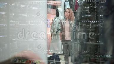 漂亮的女孩在商店里试穿一件时髦的夹克。 购物。 从窗口观看